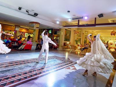 Dancers in traditional attire perform a flamenco dance in a festive indoor setting.