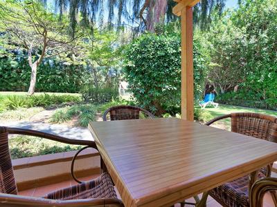 Buitenterras met houten tafel en rieten stoelen omringd door groen en bomen.