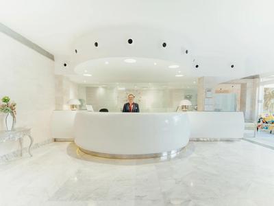Nowoczesna, jasna recepcja hotelowa z okrągłym białym biurkiem i recepcjonistą.
