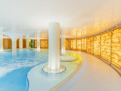 Wnętrze hotelu z jasnym podgrzewanym basenem i ciepło oświetlonymi ścianami.