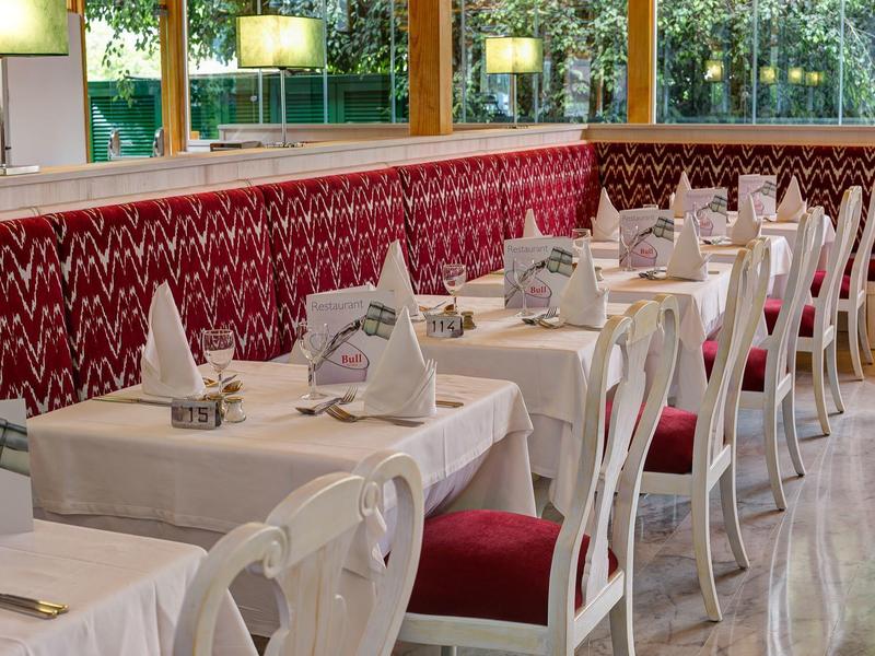 Elegant restaurant met witte tafelkleden, rode stoelkussens en grote ramen.