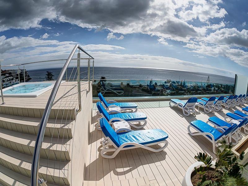 Dakterras met zwembad, ligstoelen en uitzicht op zee onder bewolkte lucht.
