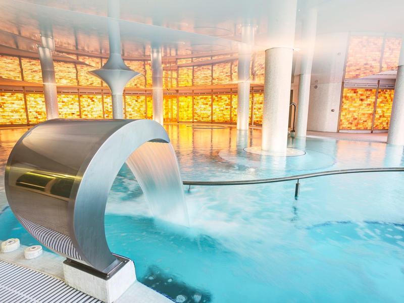 Moderne binnenzwembad met waterval en warme verlichting op de achtergrond.