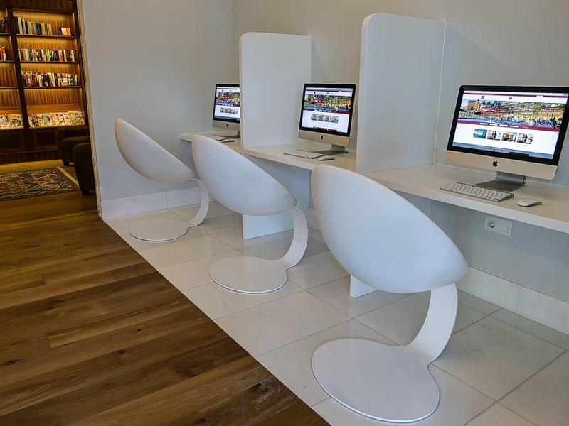 Moderne computerhoek met witte stoelen en Macs in een lichte kamer.