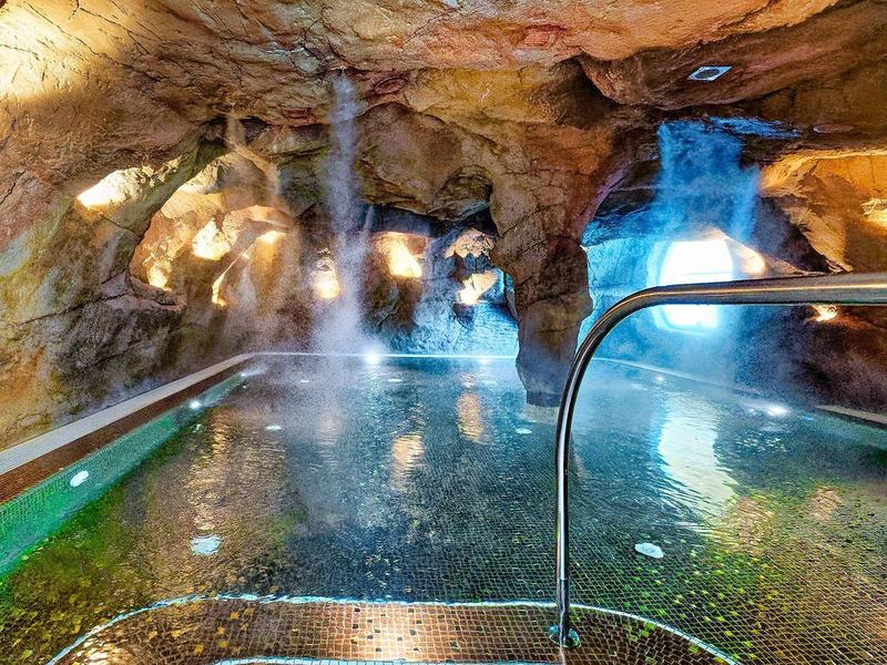 Indoor spa zwembad in een grottachtige ruimte met waterstralen en warme verlichting.