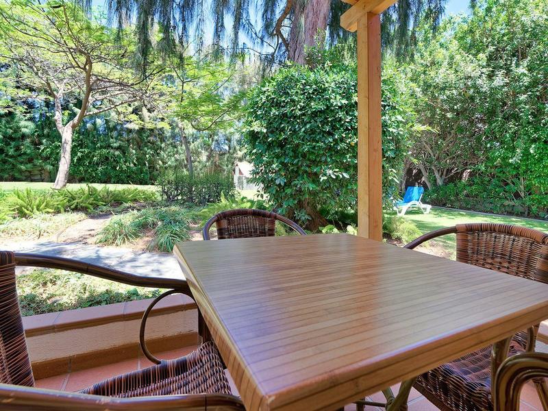 Buitenterras met houten tafel en rieten stoelen omringd door groen en bomen.