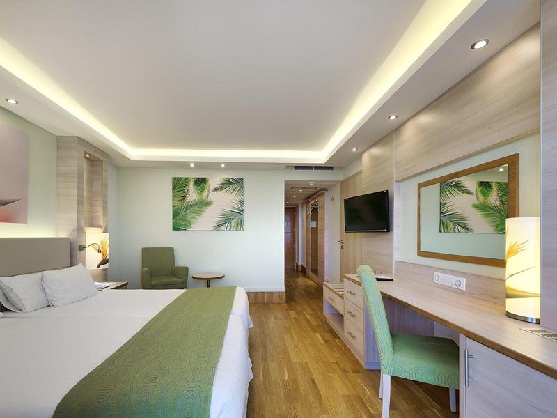 Lichte hotelkamer met houten vloer, tweepersoonsbed, bureau, stoel en moderne inrichting.