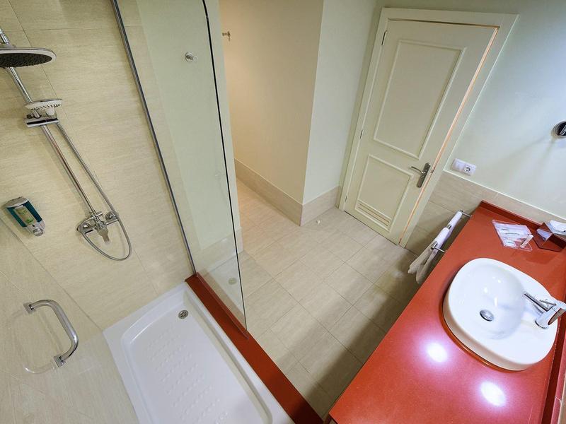 Moderne badkamer met douche, twee wastafels op rode aanrecht en beige tegelvloer en muren.