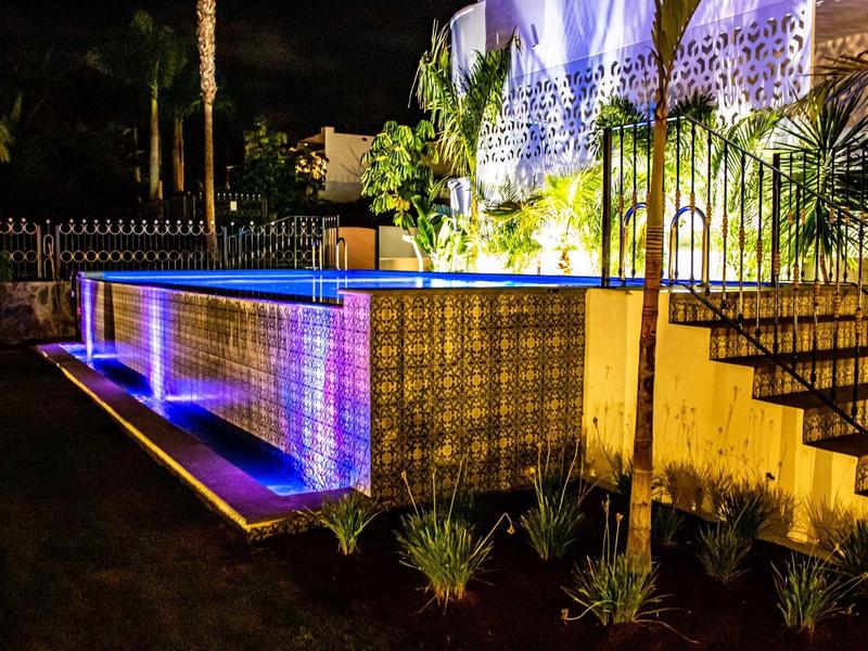 Oświetlony obszar basenu ze schodami i roślinami ogrodowymi w nocy.