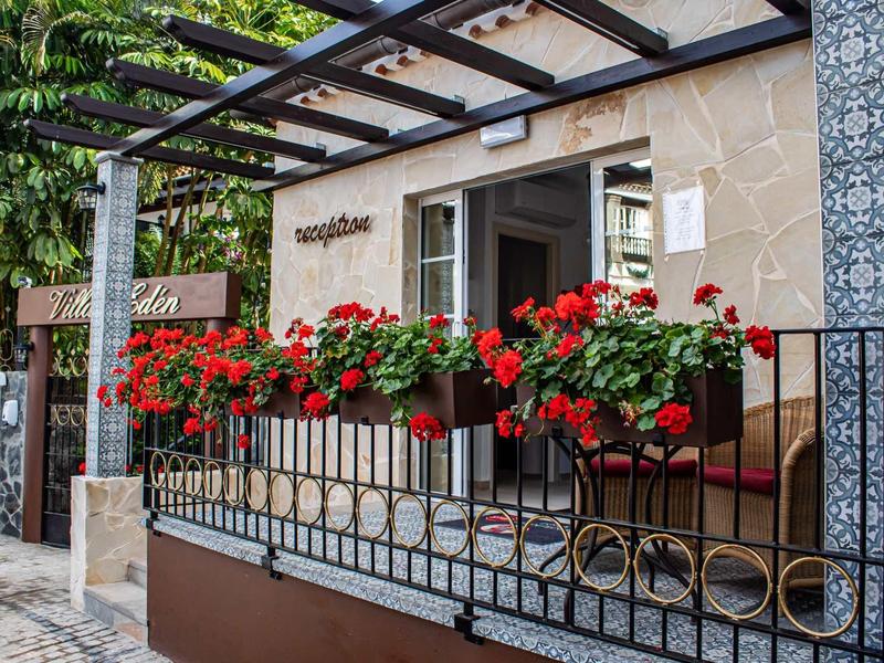 Wejście do domu z czerwonymi kwiatami w doniczkach na balustradzie przed kamiennym murem.