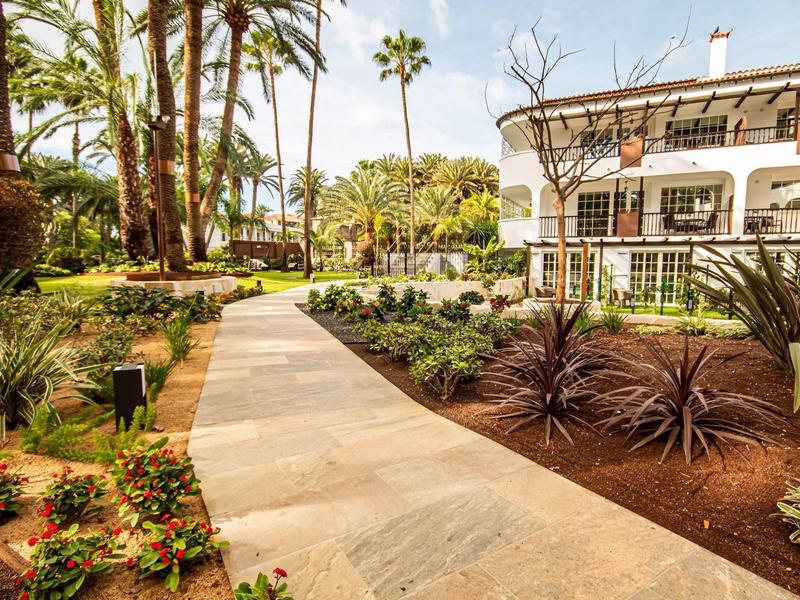 Wybrukowana ścieżka w zadbanym ogrodzie hotelowym z palmami i kwiatami.