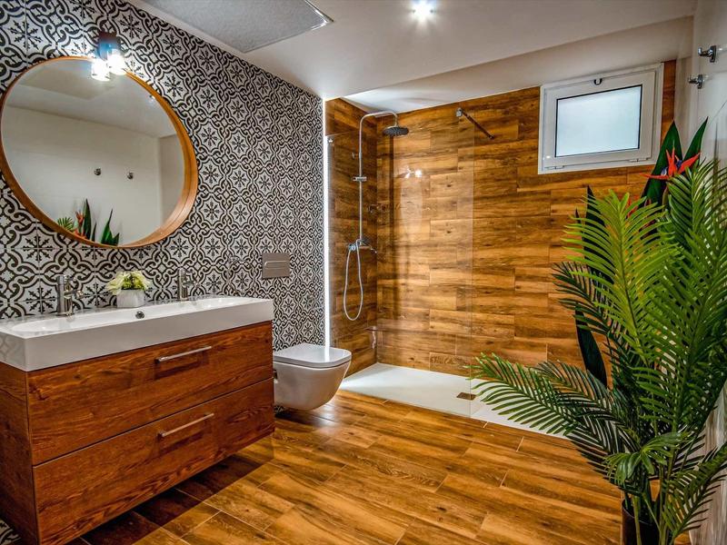Nowoczesna łazienka z drewnianą okładziną, dużym okrągłym lustrem i zieloną rośliną.