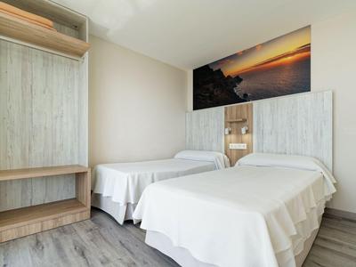 Pokój hotelowy z dwoma pojedynczymi łóżkami, drewnianymi meblami i zdjęciem zachodu słońca na ścianie.