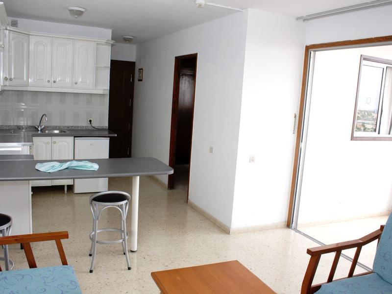 Jasny pokój hotelowy z aneksem kuchennym, meblami drewnianymi i metalowymi, z dostępem do balkonu.