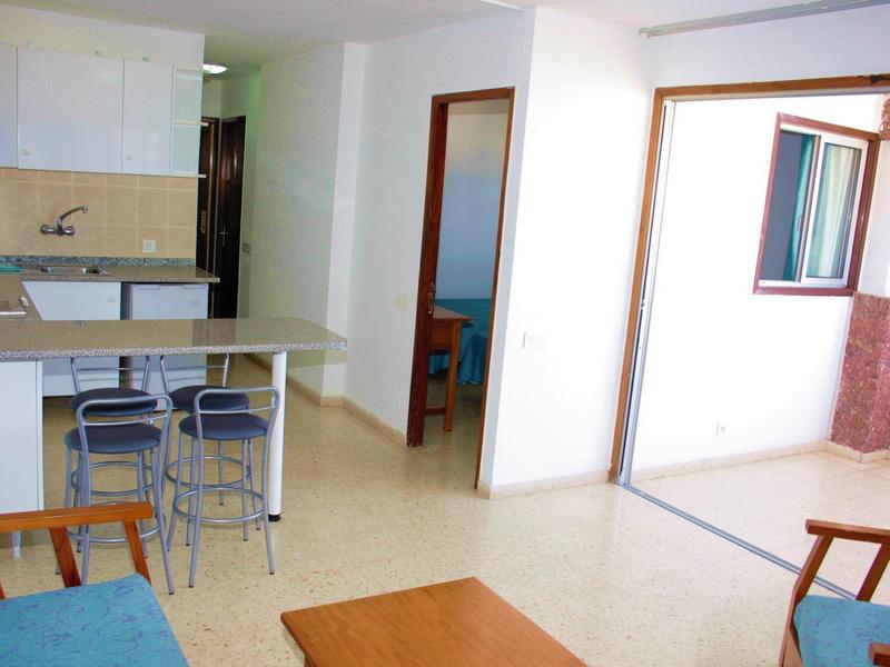 Minimalistyczny pokój dzienny z aneksem kuchennym i miejscami do siedzenia przy dużym oknie.