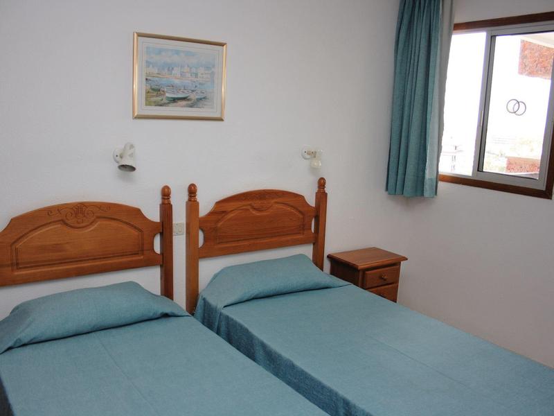 Prosty pokój z dwoma pojedynczymi łóżkami, drewnianymi meblami i oknem z zasłoną.