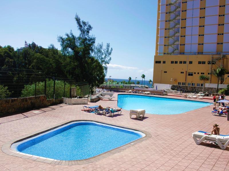 Strefa basenowa hotelu z dwoma basenami, leżakami i widokiem na drzewa i budynek.