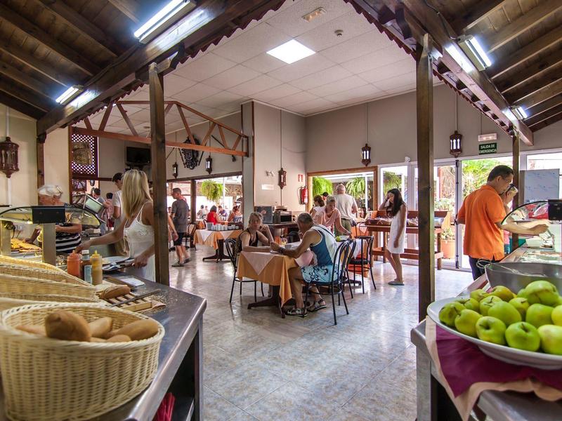 Wnętrze zatłoczonej kawiarni z gośćmi i koszami owoców na pierwszym planie