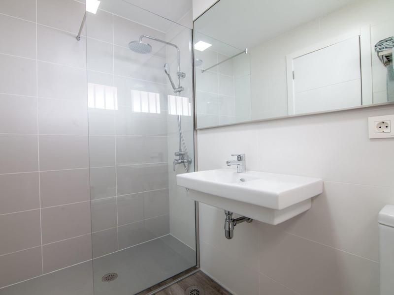 Nowoczesna, prosta łazienka z szklaną kabiną prysznicową i białą umywalką.