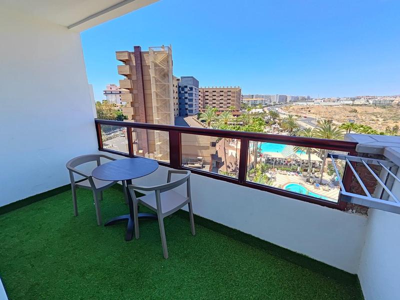 Balkon z sztuczną trawą, stołem i dwoma krzesłami z widokiem na miasto i basen.