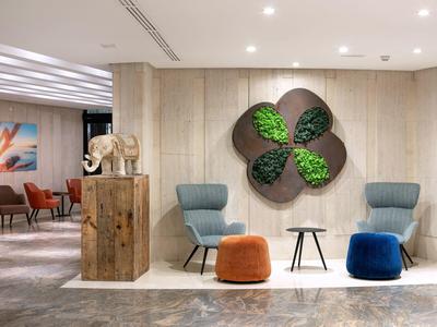 Espace lounge moderne d'hôtel avec fauteuils confortables et décoration murale végétale.