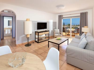 Salon lumineux avec canapé, TV, table à manger et vue sur terrasse et mer.