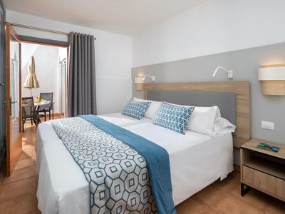 Chambre d'hôtel moderne avec lit double, accents bleus et balcon avec chaises.