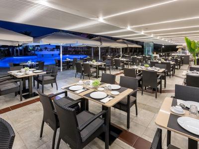 Restaurant moderne en terrasse extérieure avec des tables élégantes et une piscine éclairée en arrière-plan.