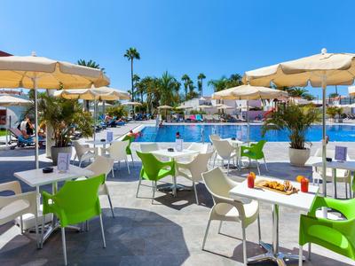 Terrasse ensoleillée avec des chaises colorées et piscine en arrière-plan dans une station de vacances.
