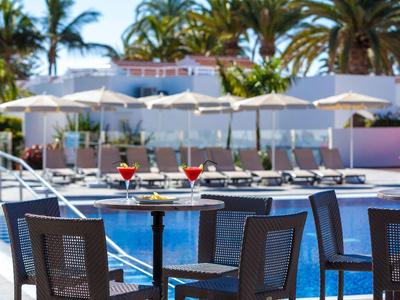 Deux cocktails sur une table près de la piscine avec des chaises longues et des parasols en arrière-plan.