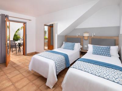 Hotelový pokoj se dvěma jednolůžky, modrými doplňky a přístupem na terasu s posezením.