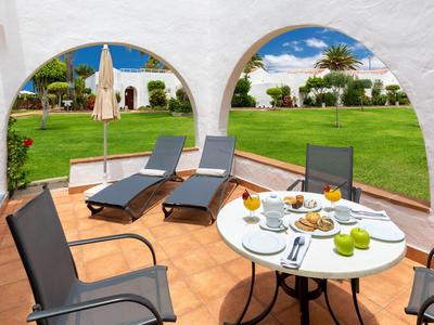 Terasa se stolem a židlemi, třemi lehátky a oblouky s výhledem na zelenou zahradu.