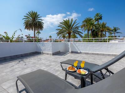 Dvě lehátka s sušenkami a nápoji na terase s palmami a modrou oblohou.