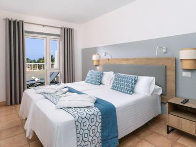 Moderní hotelový pokoj se dvěma oddělenými postelemi, modrými doplňky a balkonem s výhledem na bazén.