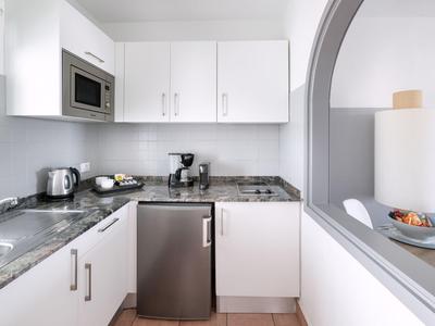 Moderní malá kuchyňka s bílými skříňkami, mikrovlnnou troubou, sporákem a mini ledničkou.