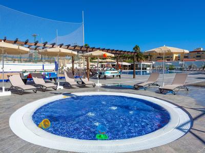 Okrągły jacuzzi na tarasie hotelowym z leżakami i parasolami pod czystym niebem.