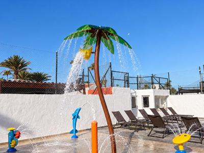 Bunte Wasserspielgeräte neben Liegestühlen in einem sonnigen Außenbereich eines Hotels.