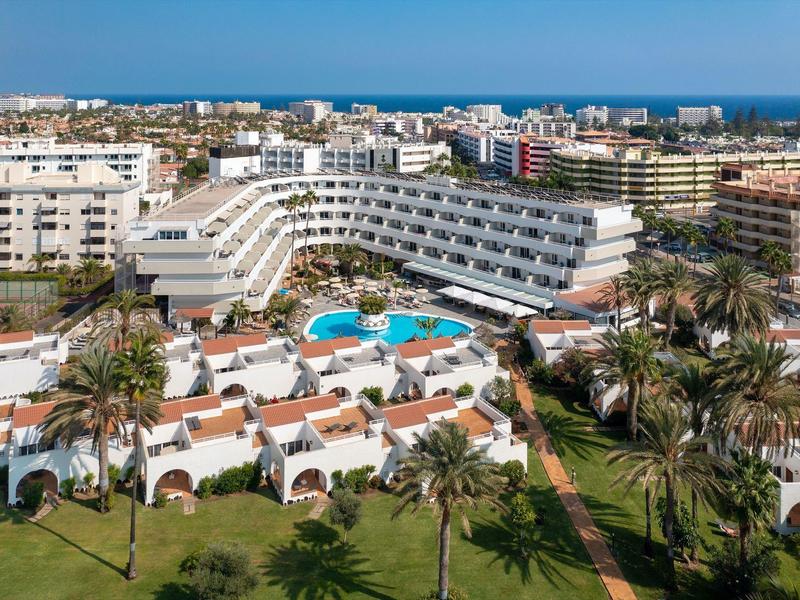 Grand hôtel avec plusieurs piscines, entouré de palmiers et proche de la mer.