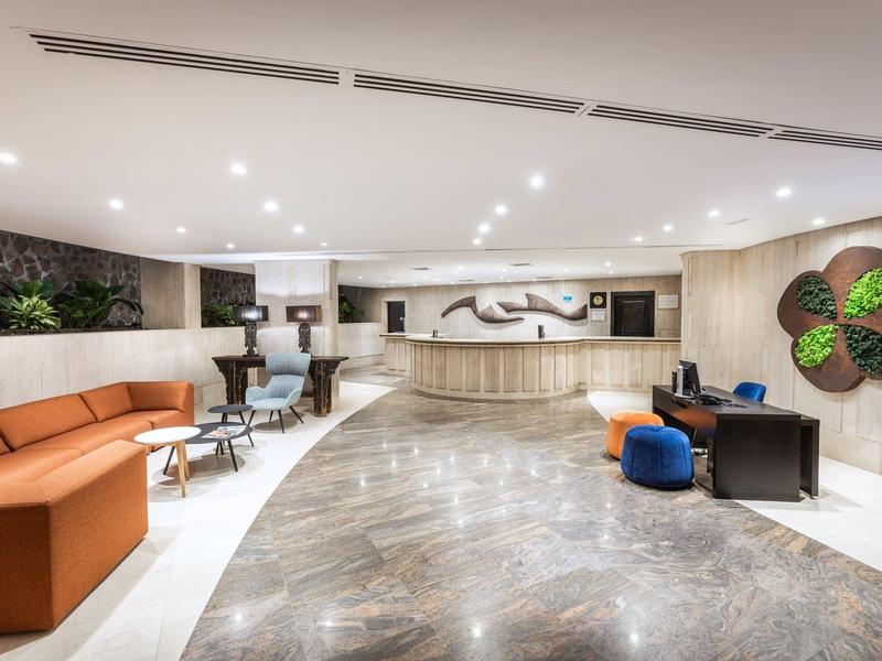 Hall d'hôtel spacieux avec comptoir d'accueil, coin salon et éclairage moderne.