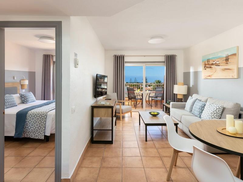 Salon lumineux avec balcon et vue sur la mer, adjacent à une chambre.