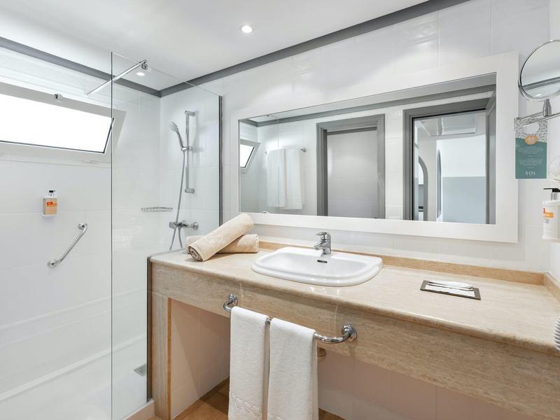 Salle de bain d'hôtel moderne avec douche, miroir, lavabo et serviettes.