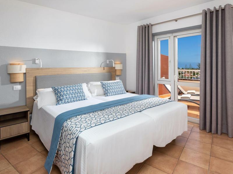 Chambre d'hôtel moderne avec grand lit double et accès au balcon avec vue sur la ville