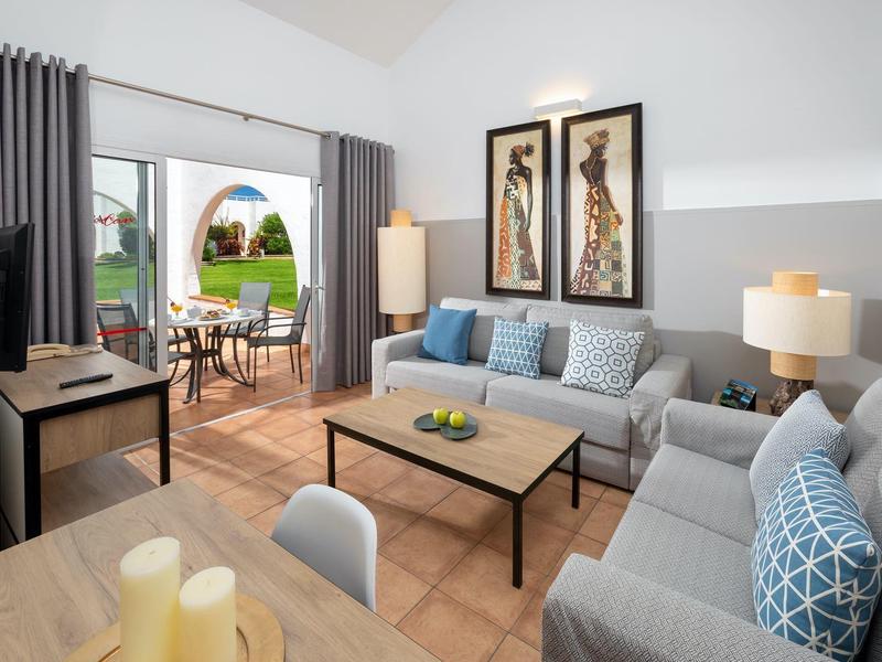 Salon lumineux avec deux canapés gris, table basse et accès à la terrasse avec vue sur le jardin.