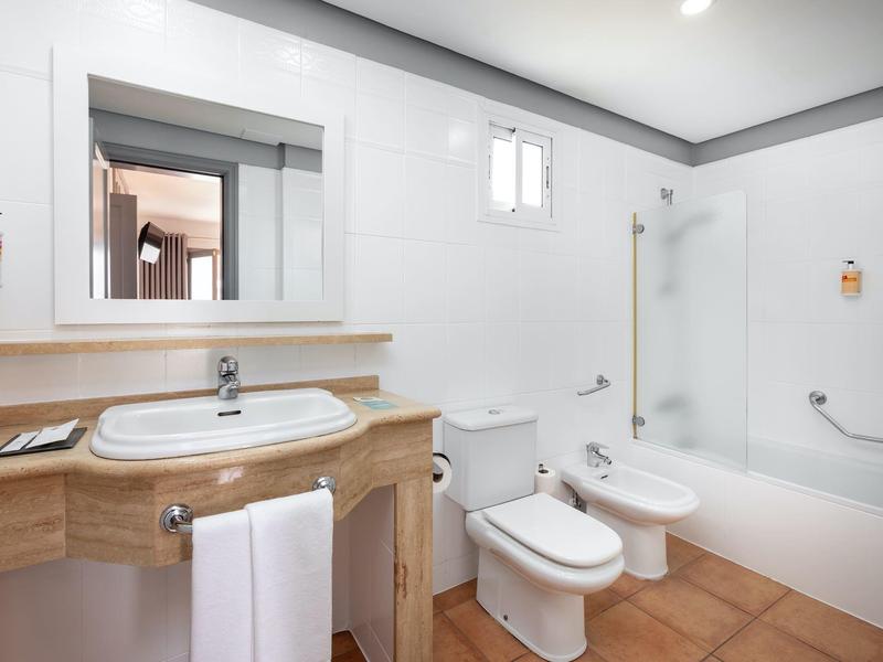 Salle de bains lumineuse avec douche, baignoire, toilettes, bidet et lavabo avec plan de travail en bois.