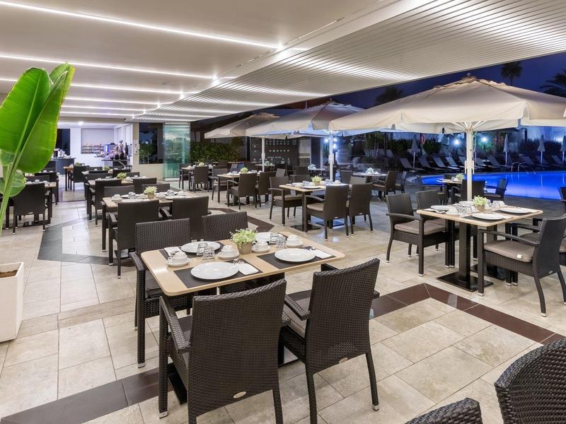 Espace repas ouvert avec tables dressées et vue sur une piscine d'hôtel