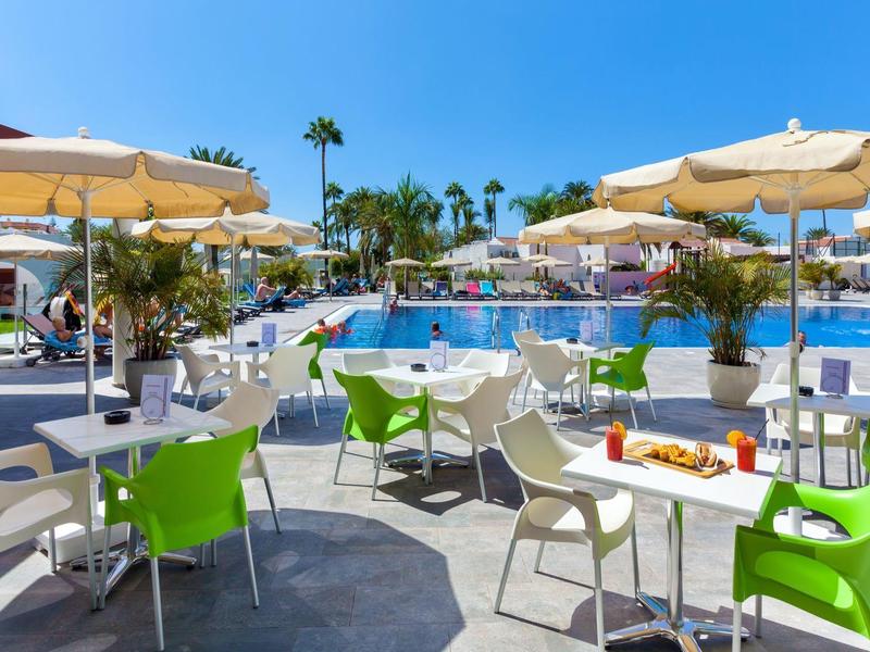 Terrasse ensoleillée avec des chaises colorées et piscine en arrière-plan dans une station de vacances.