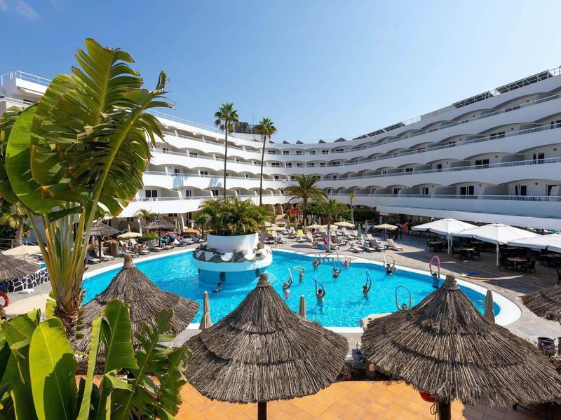 Hôtel moderne avec grande piscine extérieure, parasols et plantes tropicales
