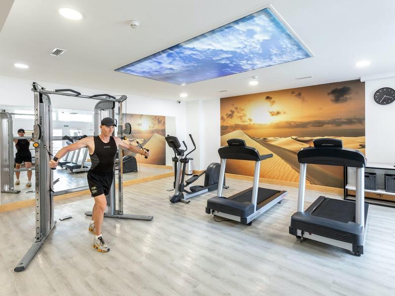 Salle de sport moderne avec tapis de course, équipements d'entraînement et grande décoration murale dans un hôtel.