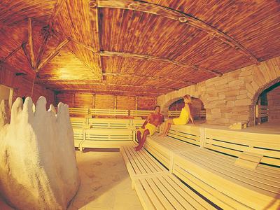 Holzsauna mit mehrstufigen Sitzbänken, holzverkleidetem Gewölbedecken und zwei entspannten Personen.