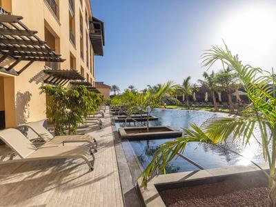 Piscine d'hôtel moderne avec chaises longues et palmiers par une journée ensoleillée.